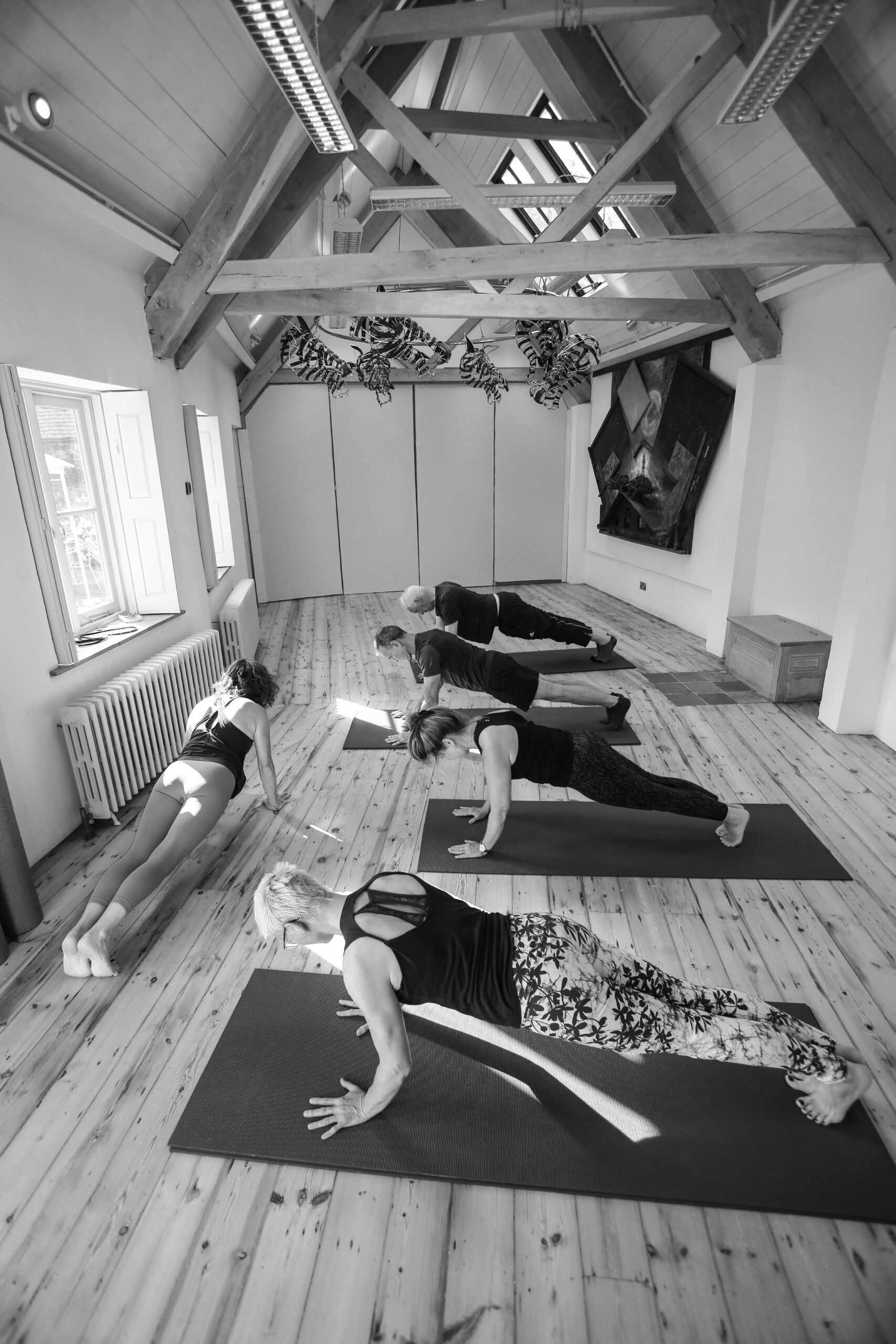 A mat class holding a plank in the North Barn studio under its timber roof
