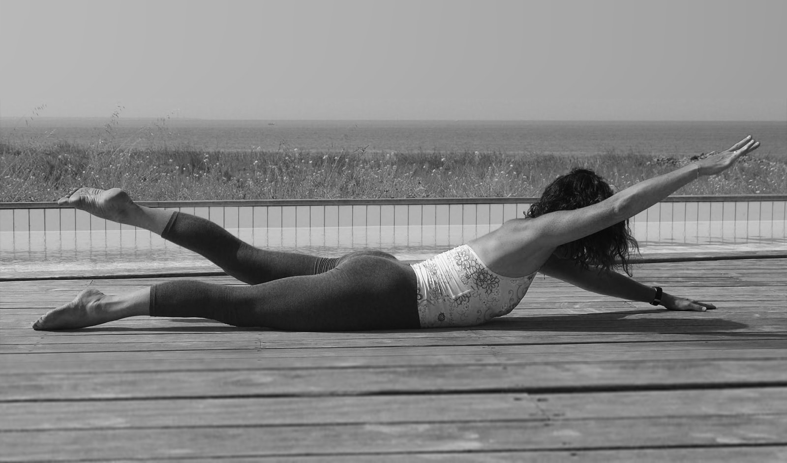 Caroline in a swan dive on a wooden deck with the sea horizon behind